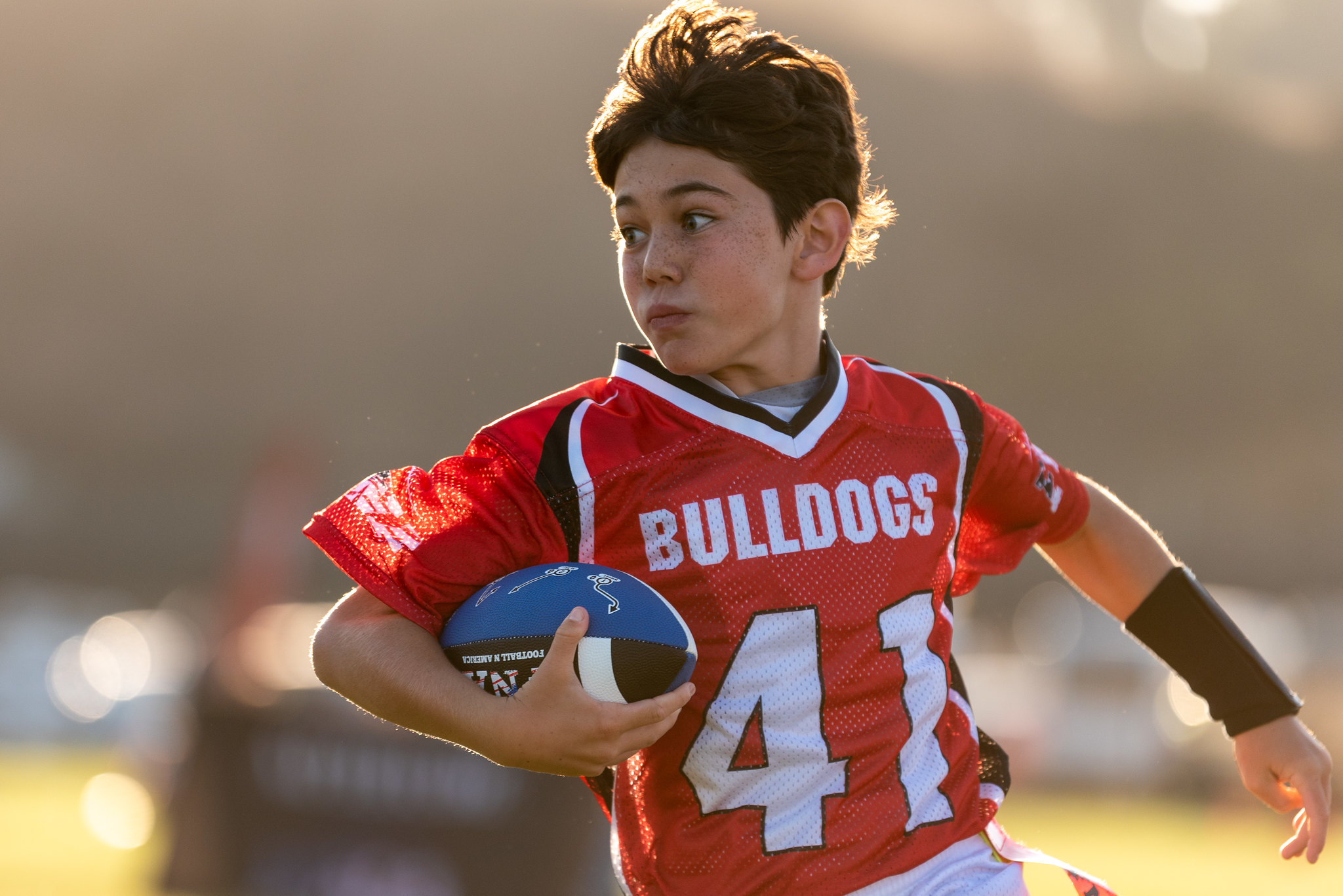 Niño jugando tocho bandera con uniforme rojo del equipo Bulldogs.